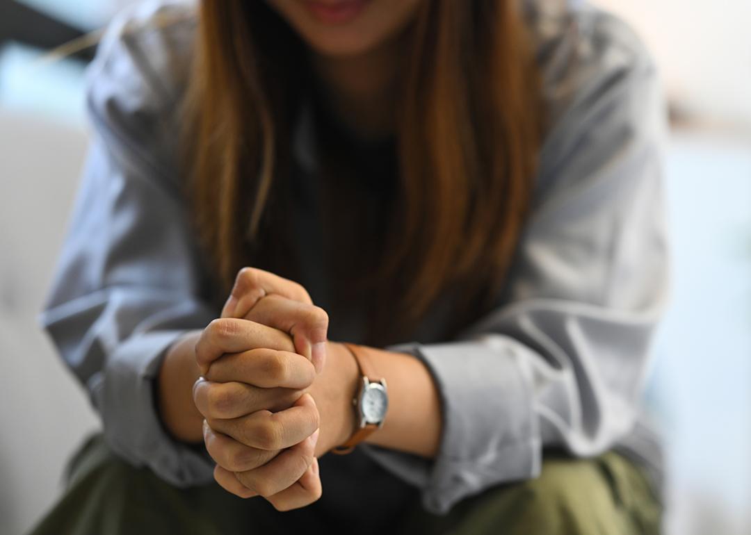 Sad woman sitting on a sofa with hands clasped.