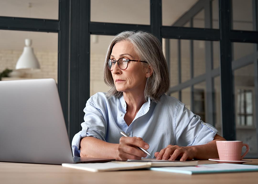 Senior woman looking up information online and writing notes.