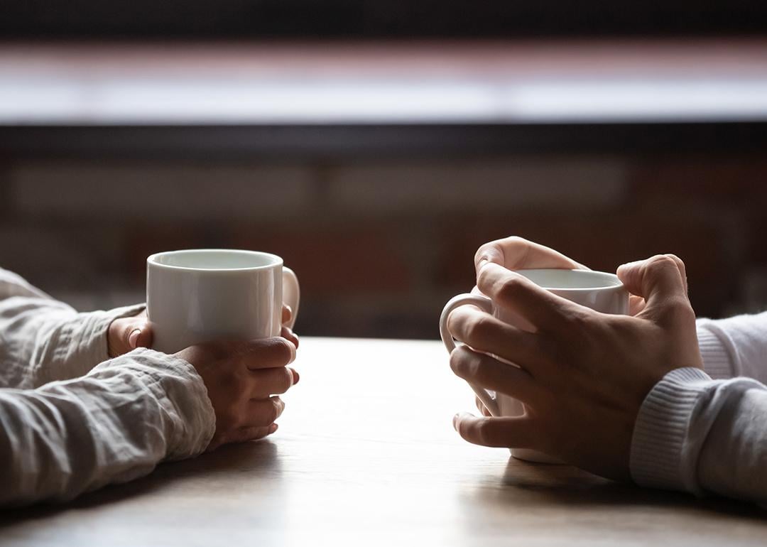 A Gen Z and Millenial sitting across each other at a table drinking coffee.