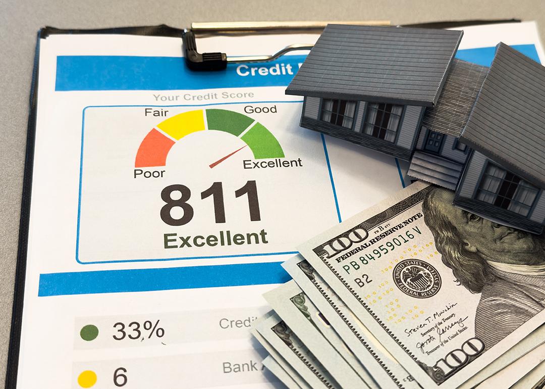 Figure of a house made of paper with credit report letters and cash around it.