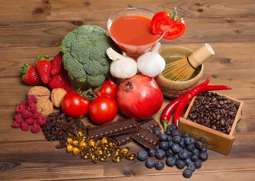 Healthy antioxidants foods like broccoli, berries, tomoatoes, pomegranates, green tea, coffee, nuts and chocolate on a wooden table.