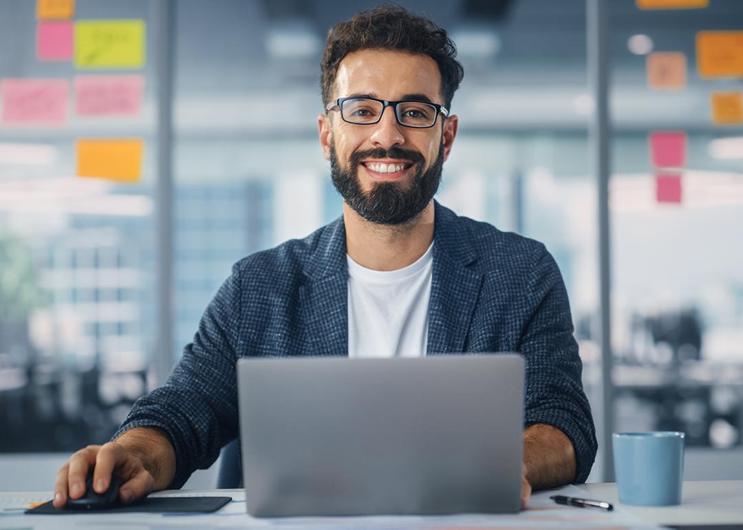 Worker in a modern office smiling while using a laptop.