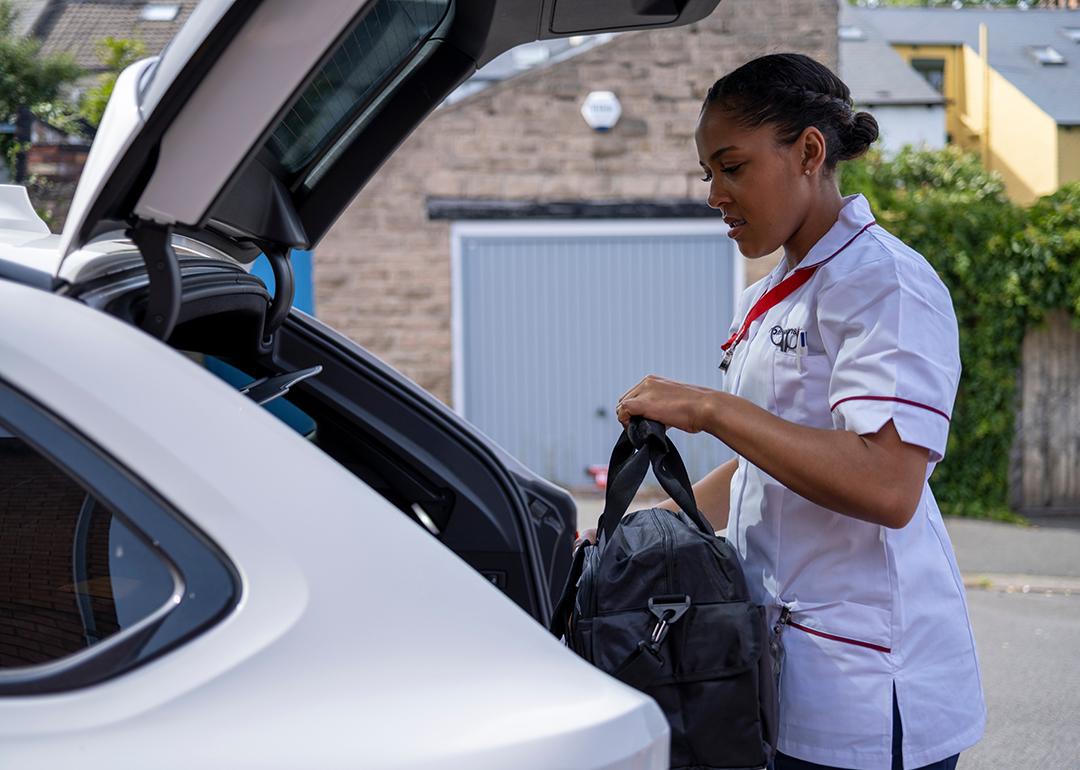 A travel nurse putting her bag in the trunk of her car.