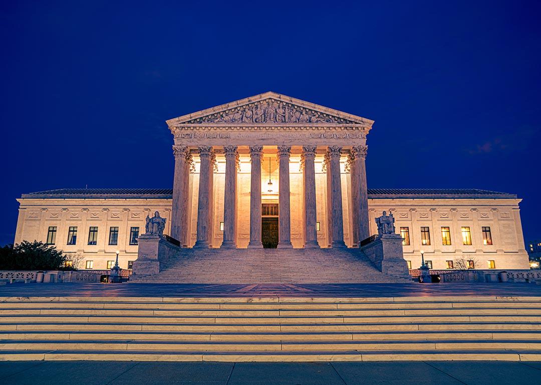 United States Supreme Courts building illuminated at night in Washington DC with steps and plaza in foreground.