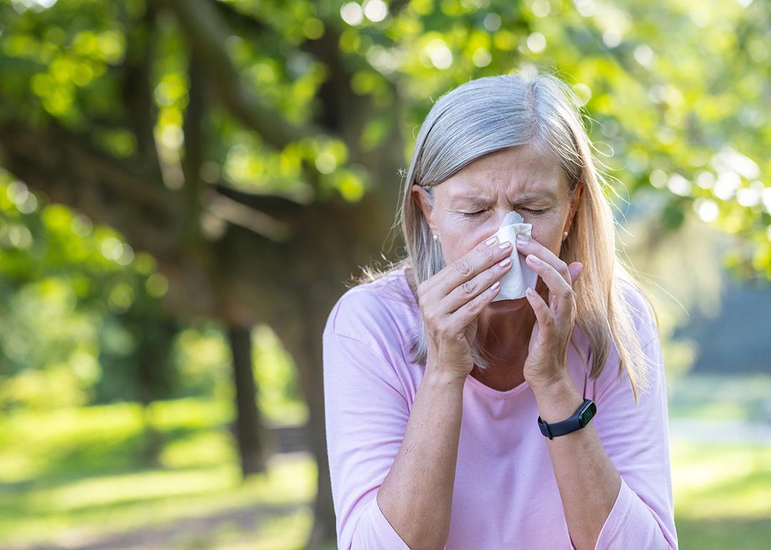 Senior woman outdoors wiping her nose with a napkin.