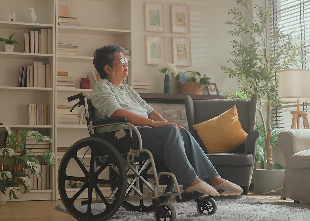 Senior woman in a wheelchair staring at a window in the living room.