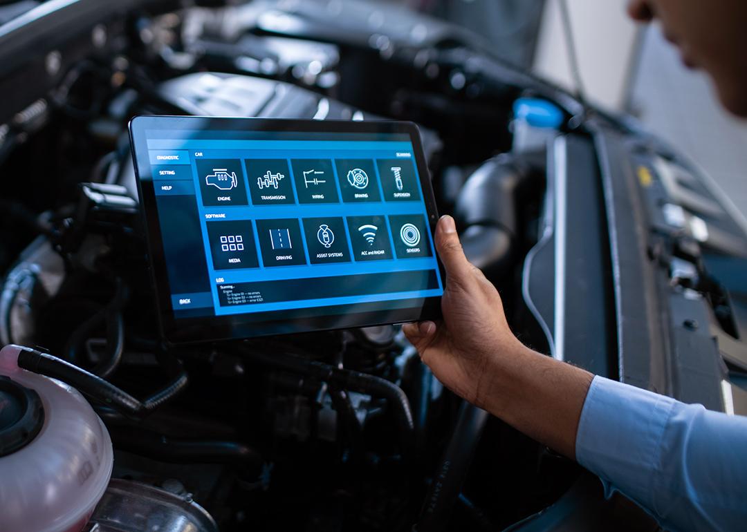 Car mechanic using a tablet to diagnose a car's components' issues.