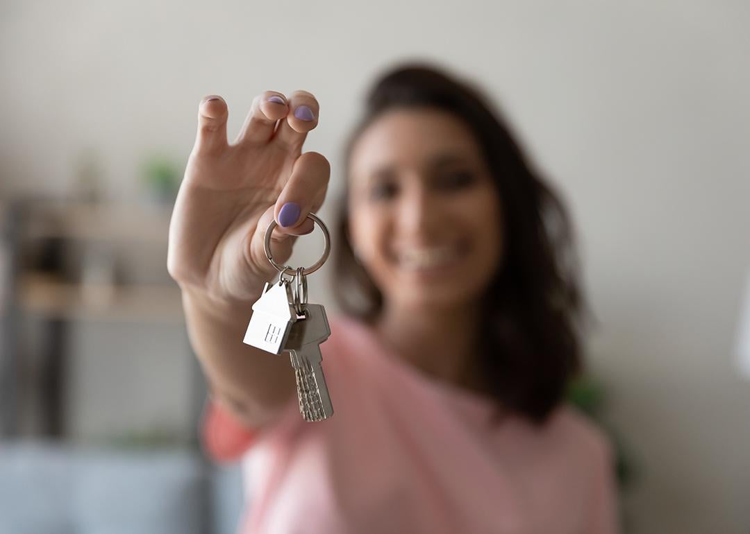 A young female homeowner holding up the keys to her house.