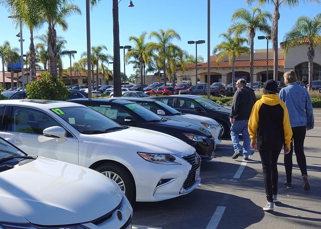 A parent and his teenagers looking at a row of used cars.
