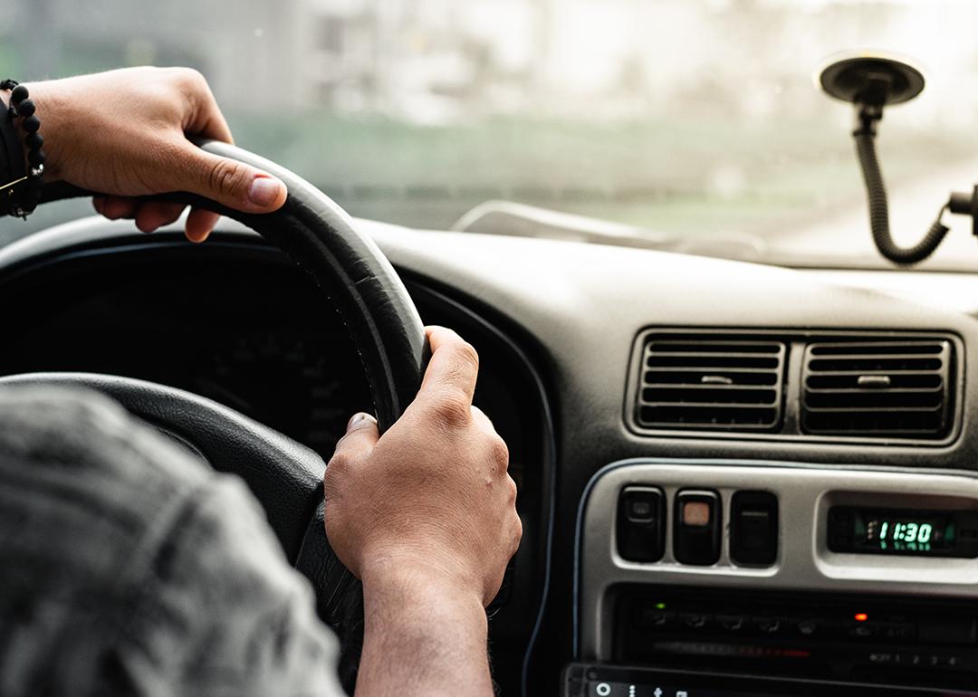 Close-up of a man holding the steering wheel while driving on the road.