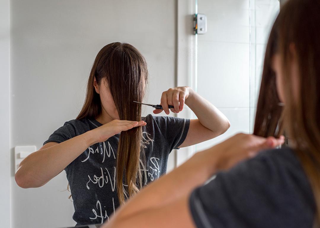 A woman cuts her hair in front of a mirror to have bangs.