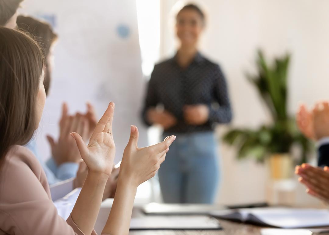 Members of a team applaud another member after a successful meeting presentation.