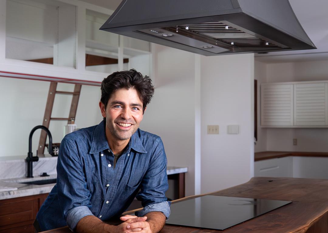 Adrian Grenier stands beneath his island-mounted CopperSmith® range hood, featuring a smooth bronze finish, paired with a handcrafted wood countertop for a warm, natural aesthetic.