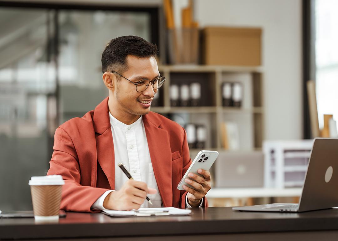 Small business owner holding a phone on his one hand and writing down information with the other.