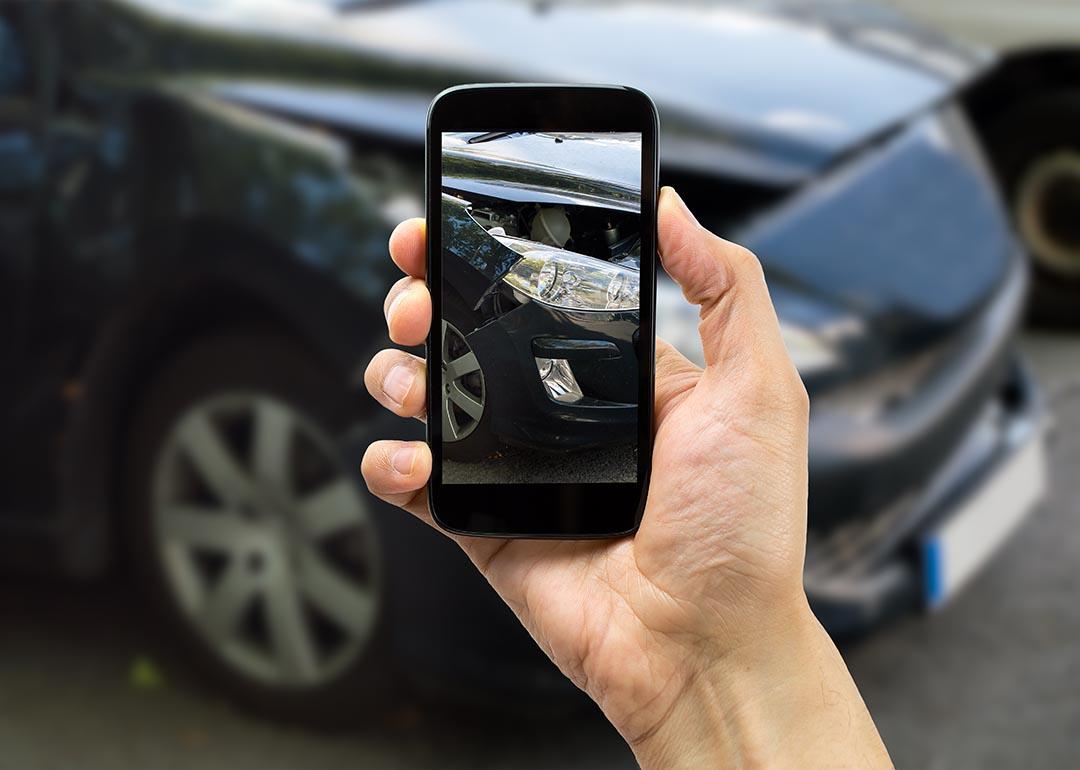 Person photographing passenger side headlight of damaged black car with smart phone for accident insurance.
