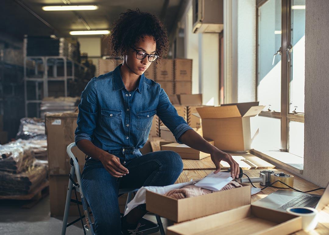 Black woman wearing denim outfit prepares packages for shipping in a fulfillment office.
