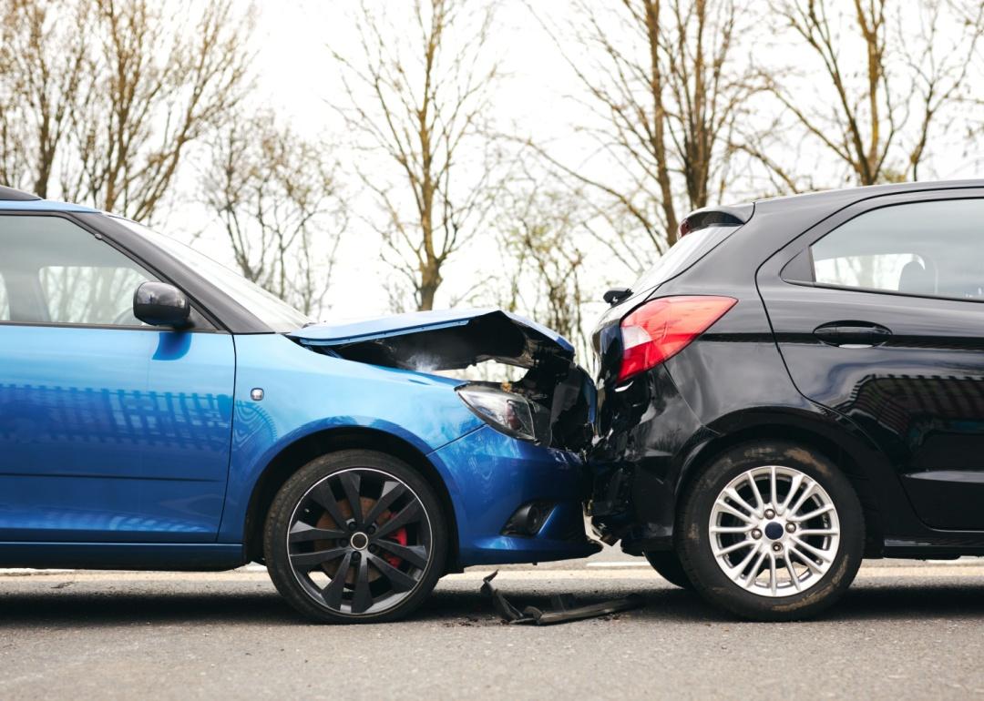 Two cars involved in traffic accident on side of the road with damage to hood and fender.
