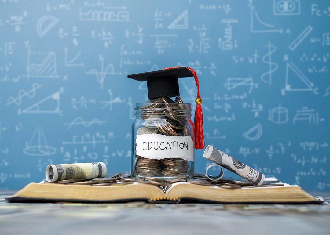 Photo illustration showing concept of college education cost with a jar of savings, a graduation cap, books and a blackboard with math in the background.