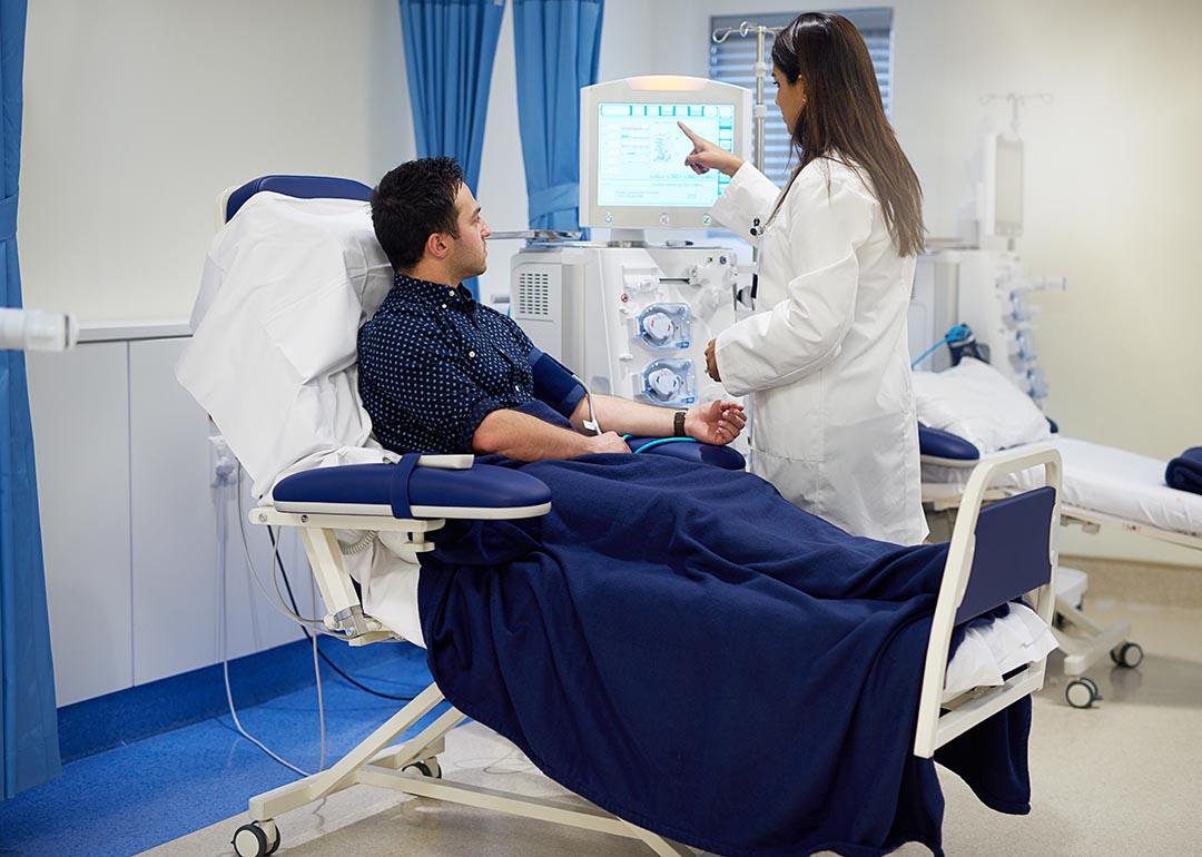 Patient sits getting hooked up to dialysis machine with nurse helping set up.