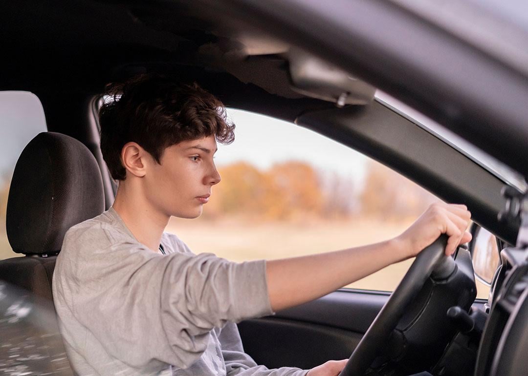 Young male driver holding steering wheel in car seen through the passenger side window.