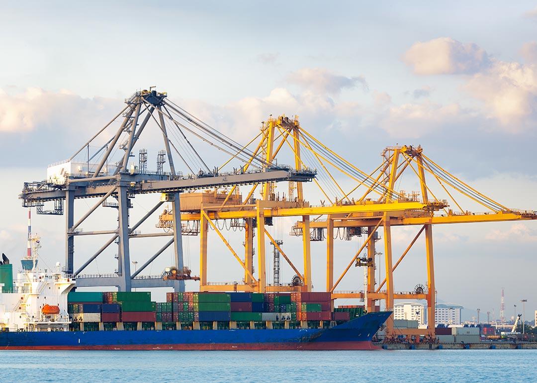 Two yellow and one gray crane with a cargo ship in a port.