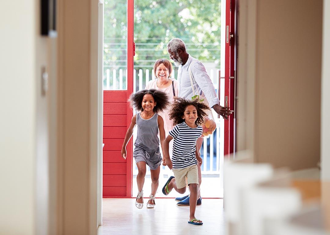 Two cute children with natural hair running into open door of house with grandparents in the background.