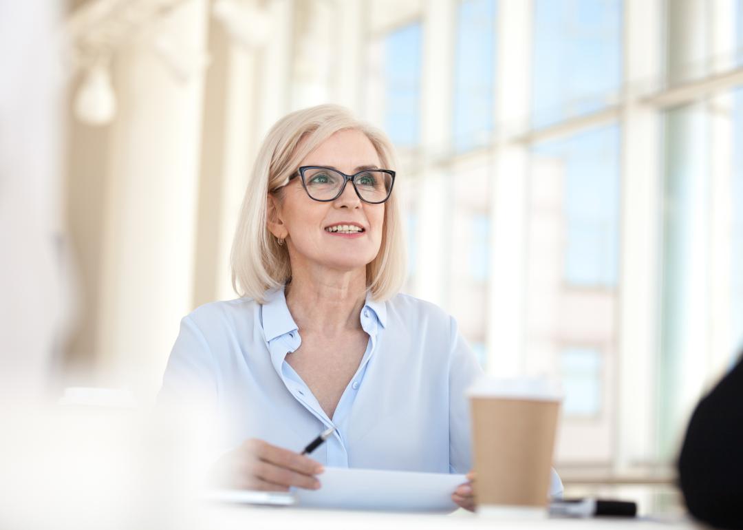 Blond professional sitting at table with large windows in the background talking in meeting.