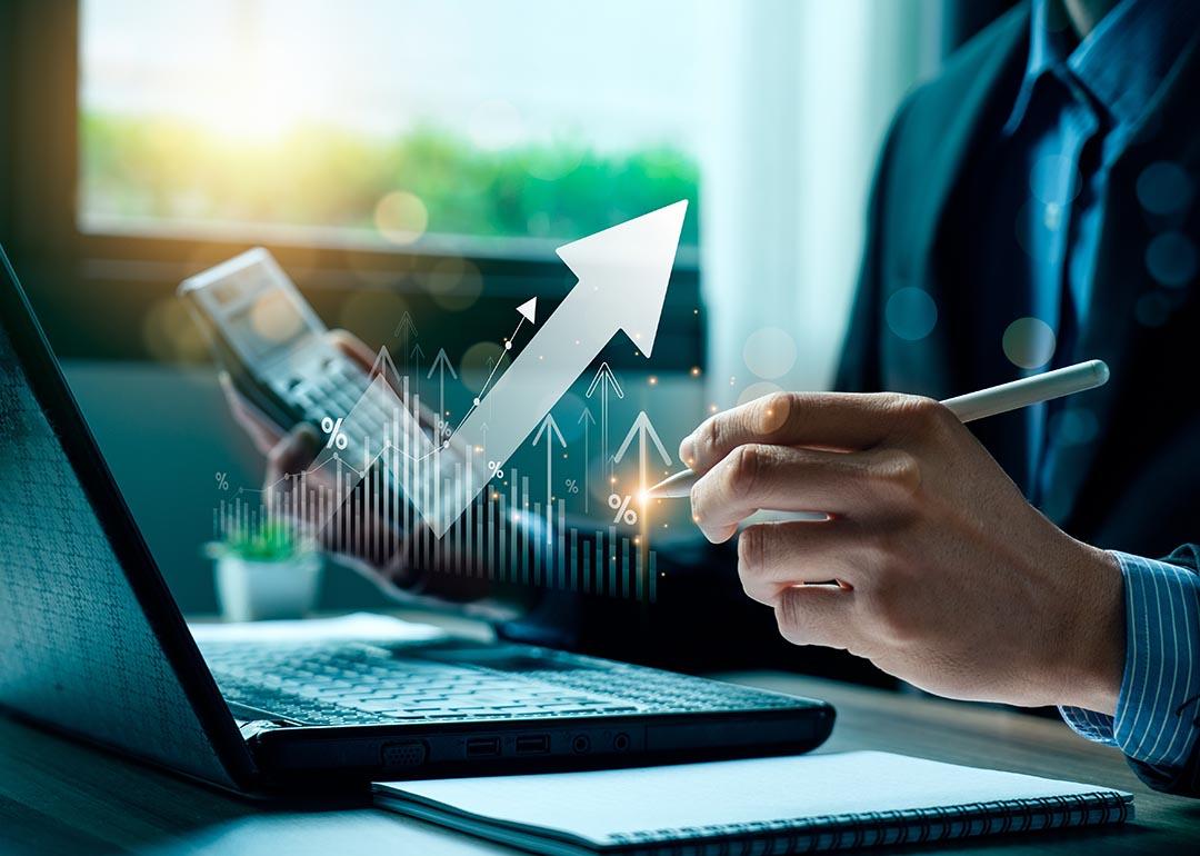 Person wearing a suit working on laptop and calculator, holding a pen with finance icons overlaid to symbolize money management.