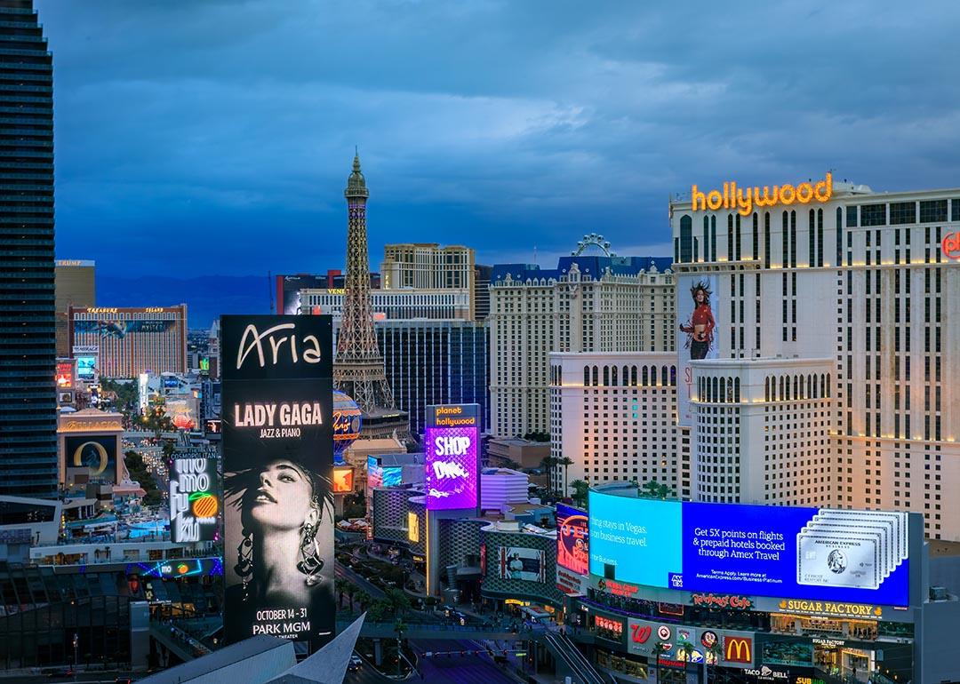 The Strip skyline in Las Vegas with advertising billboards including Lady Gaga, neon lights on iconic hotels and casinos after sunset.