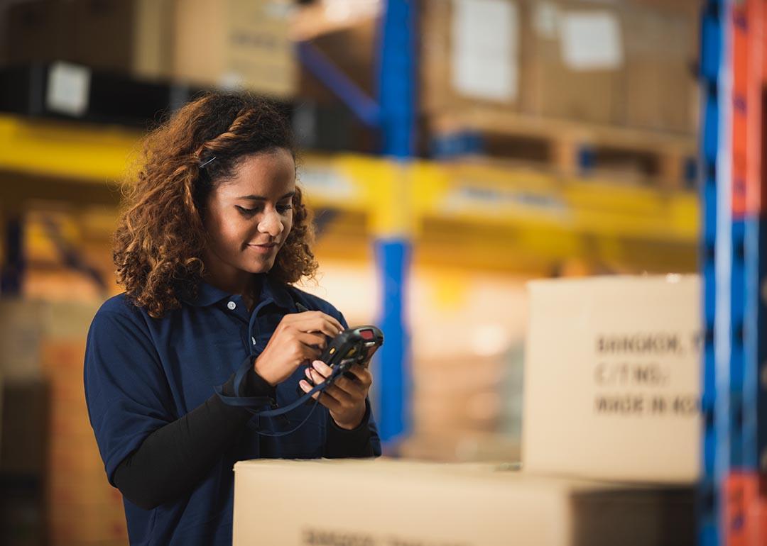 Warehouse worker using bar code scanner on boxed goods inside warehouse.