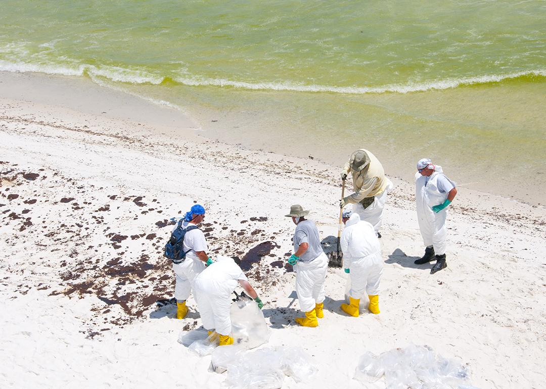 A group of BP oil workers attempt to clean sand spilled with oil in Pensacola Beach, Florida.