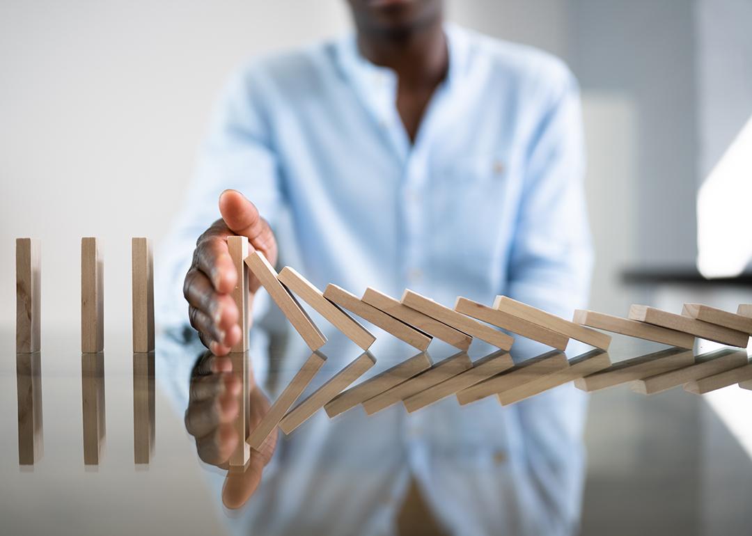 A businessman stopping a row of domino wooden bricks with his hand.