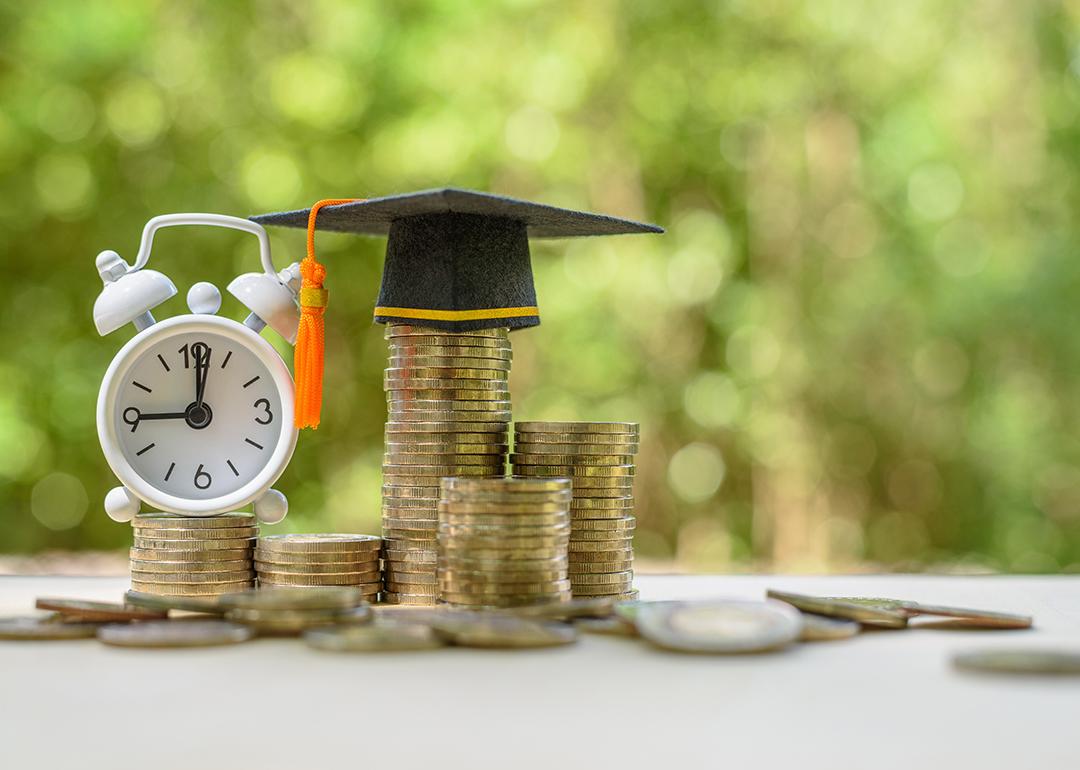 A clock and graduation cap on top of coins as a concept of student loans.