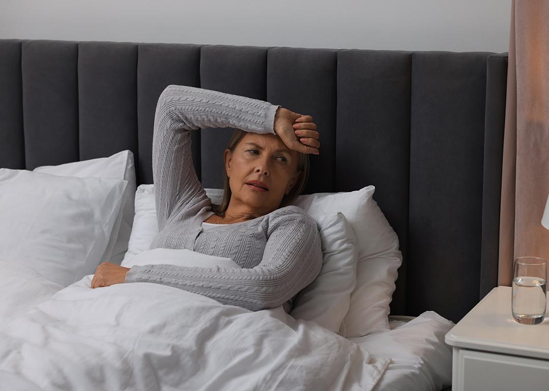 A middle-aged woman experiencing headache while sitting on bed.