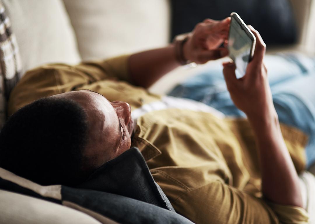 Young man relaxing on a couch at home while scrolling through social media on his phone.