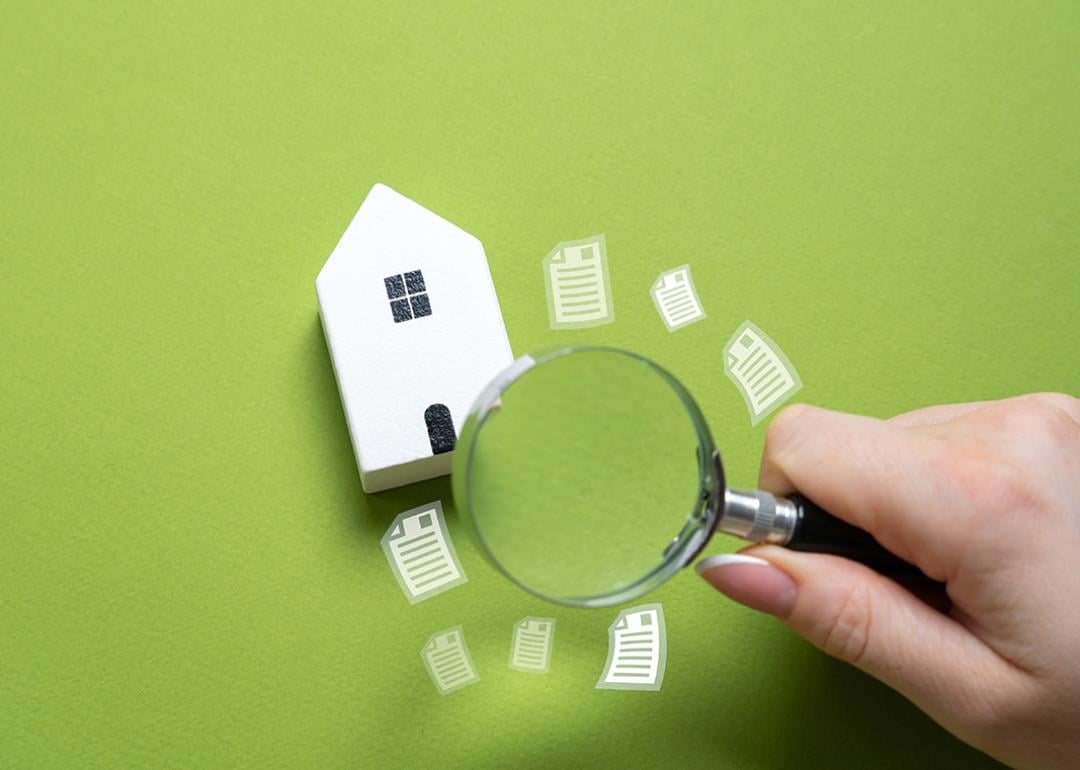 A magnifying glass looking over a figure of a house on a green background.