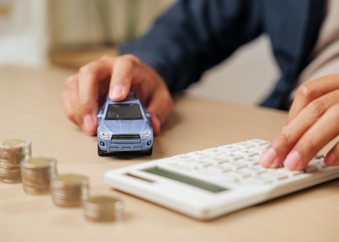 Calculator in hand as a person calculates car loan payments by a small car model and coins. 
