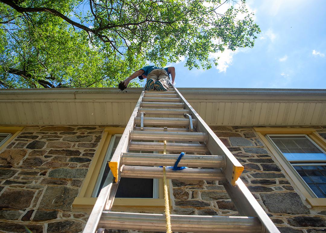 Low angle view of a man on a ladder cleaning a home's gutters.