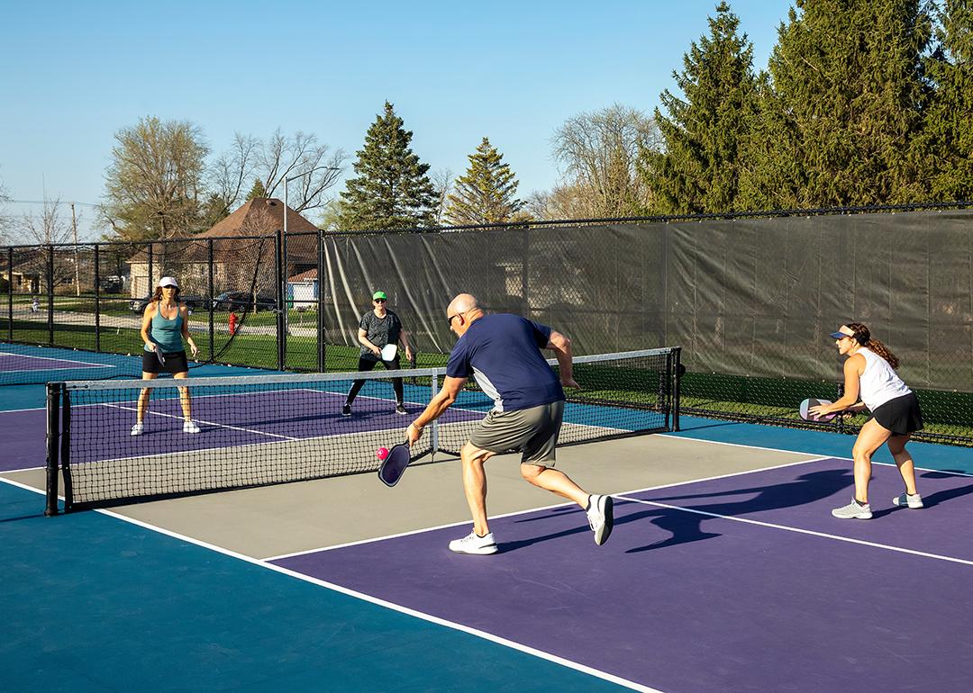 Two teams playing at a public park's pickleball court where a male player returns a volley at the net.