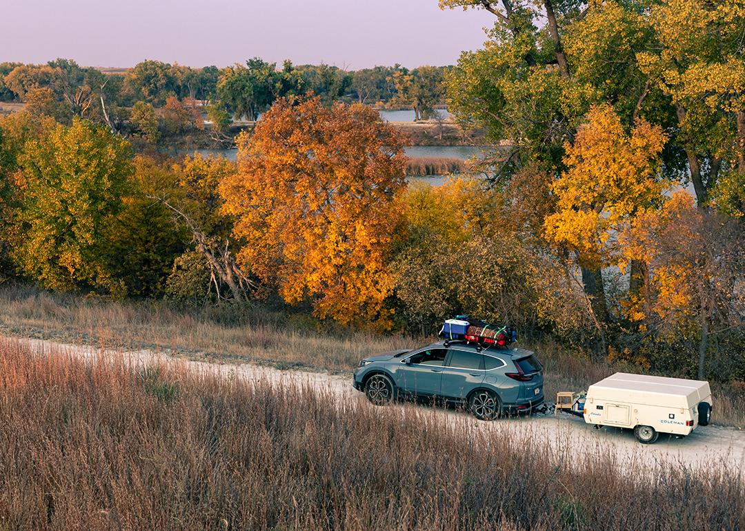 A blue 2020 Honda CR-V towing a 1990 Coleman Columbia pop-up camper on the road towards Antelope Lake in Kansas during autumn.