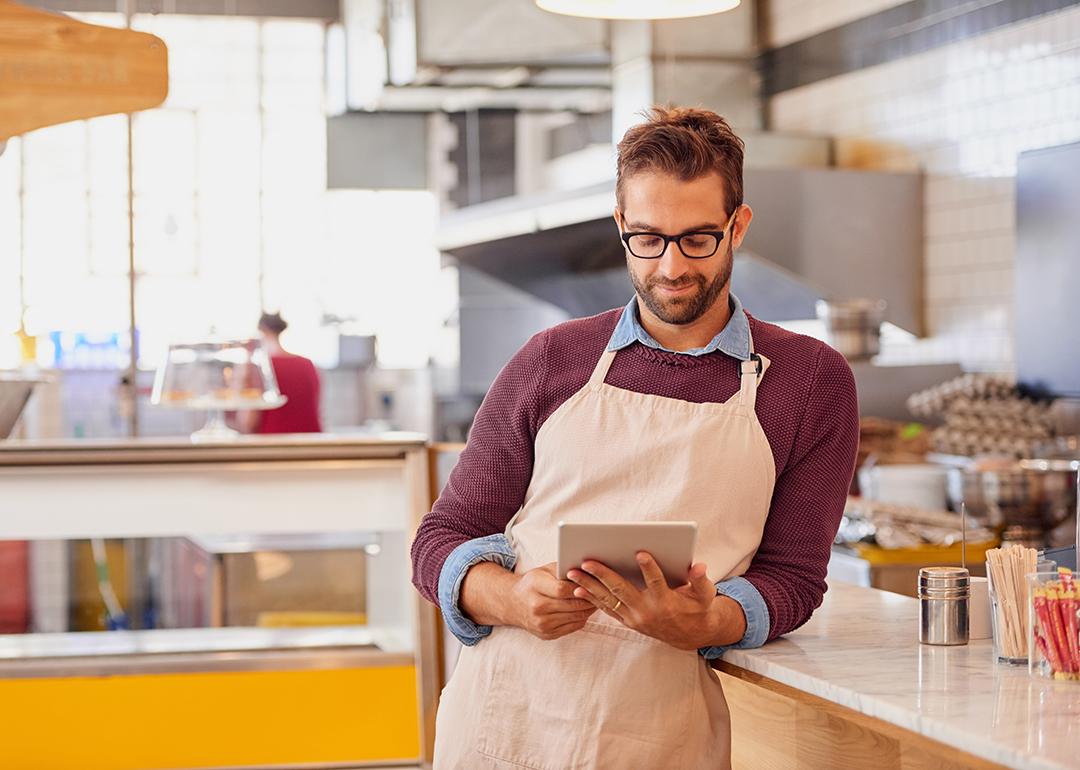 A coffee shop owner using a tablet inside the shop's kitchen.