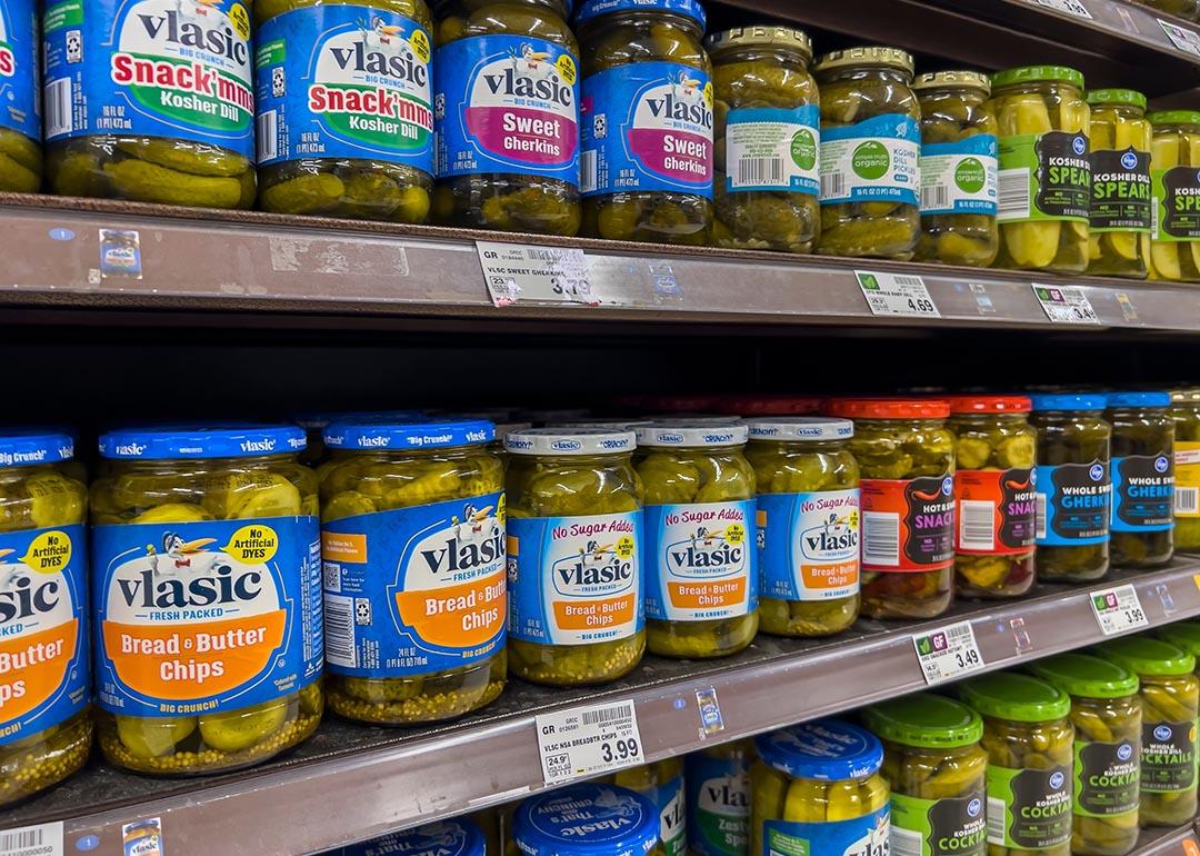 Close up of three shelves of jars of pickles starting with vlasic brand for sale in a grocery store.