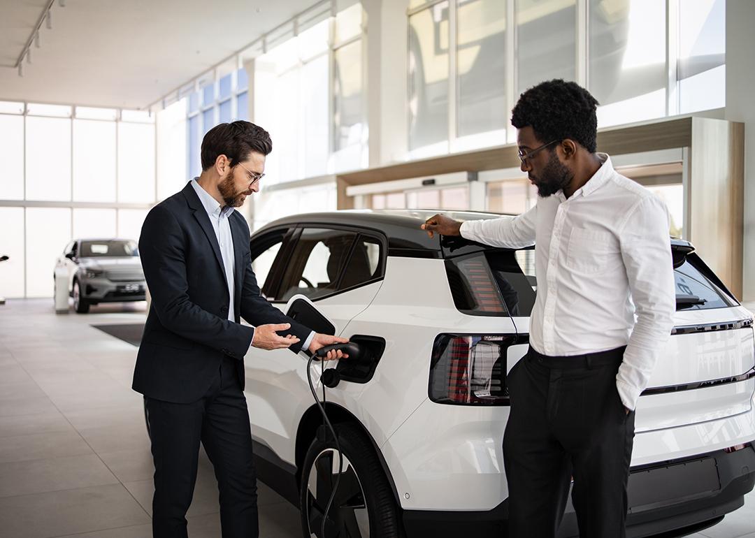 A dealer selling a white electric SUV to businessman in a car dealership.