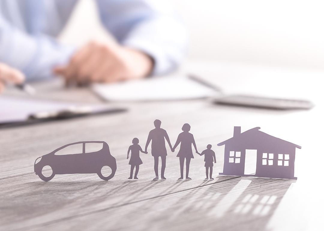 an insurance agent writing in documents with a paper figure of a family with a house and car.