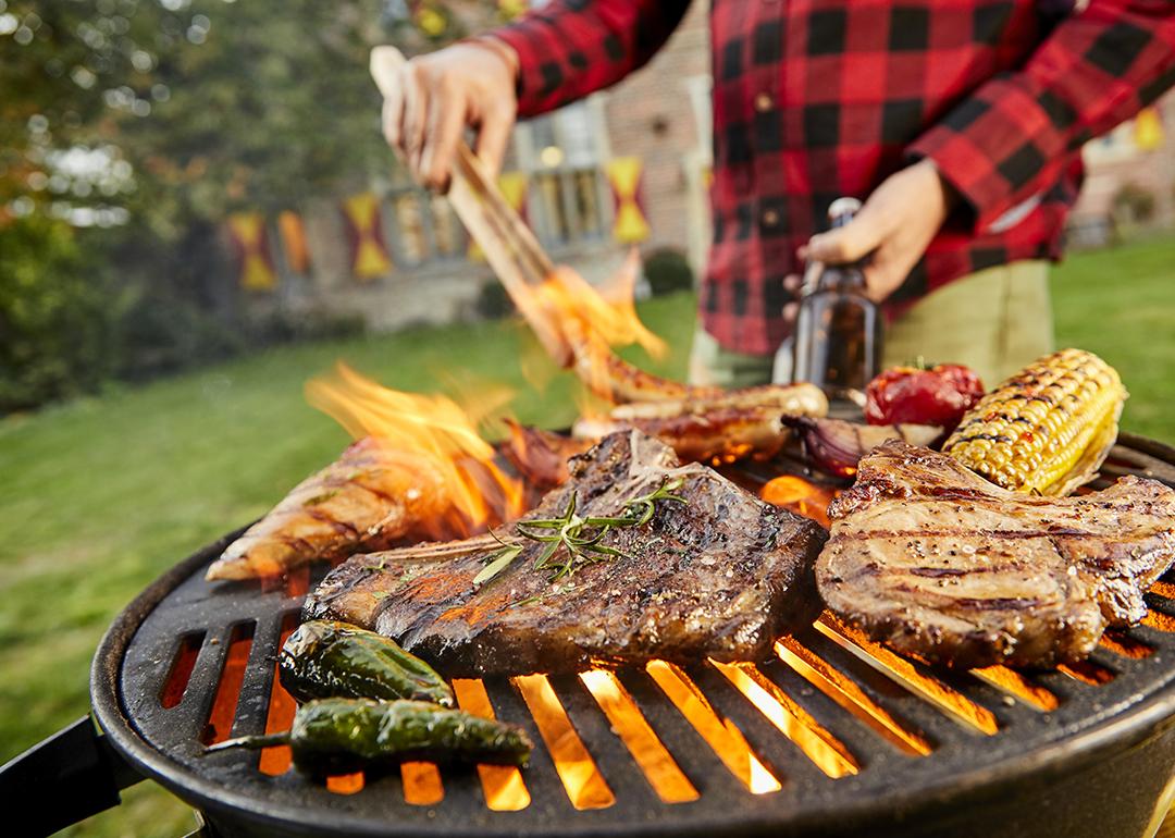 Assorted meat like sausages and steak with vegetables being grilled on a BBQ grill outdoors.