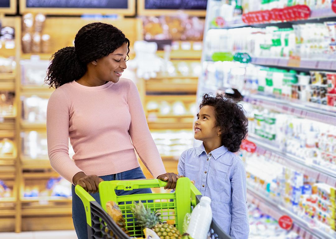 A young black mom and her daughter shopping together for groceries in a supermarket.