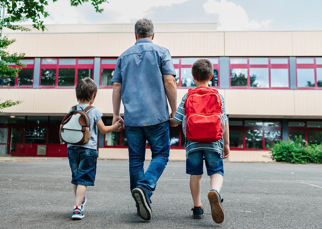 A father holding his two young boys and dropping them back to school.