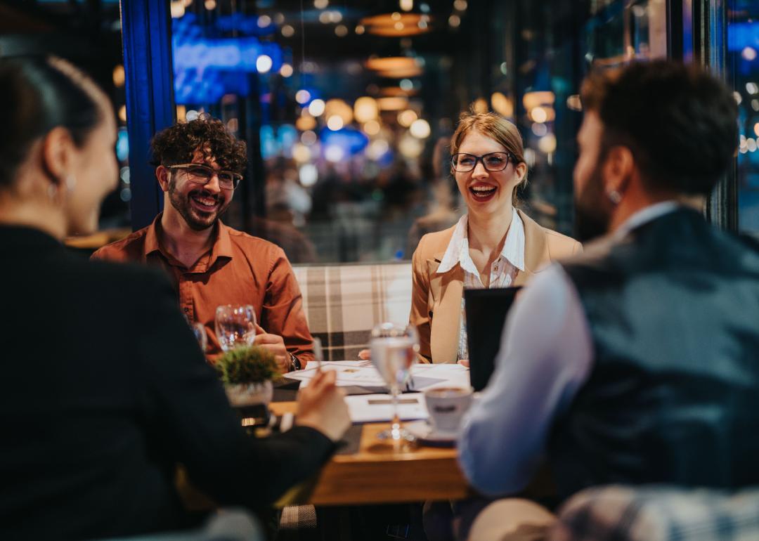 A group of business people laughing and discussing during a meeting in a modern restaurant setting.