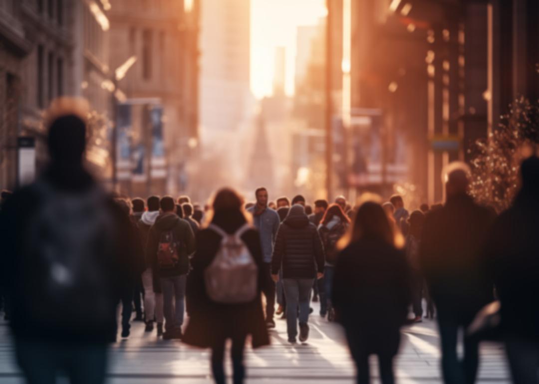 A crowd of people walking in a city street during sunset.