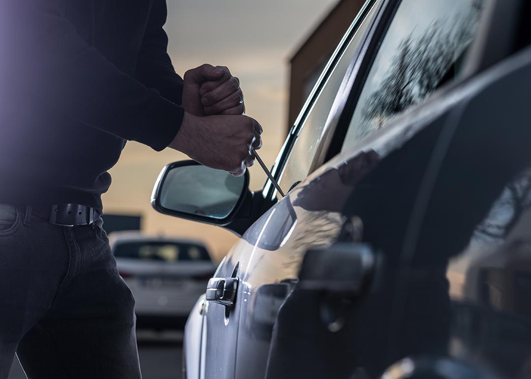 A thief trying to break into a car window with a screwdriver.